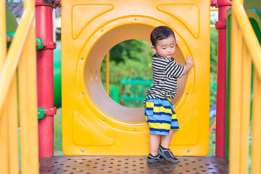 Sad Asian boy playing in yellow tunnel at the playground with su