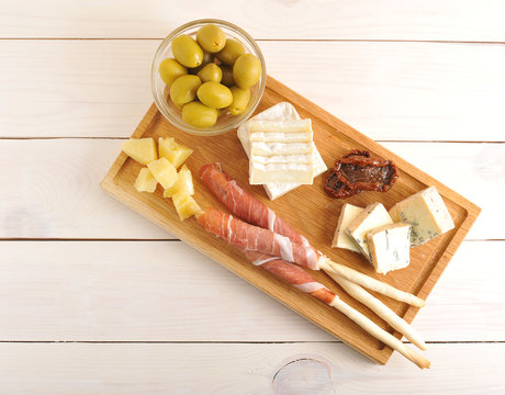 bacon on bread sticks, cheese, dried tomatoes, olives on a woode