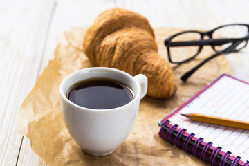 French croissant, glasses, cup of coffee and notebook