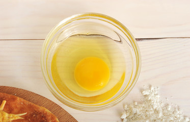 raw broken egg in a glass container on wooden background
