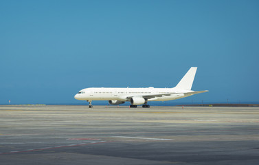 White aircraft stands on the airport field, in front of a blue sky
