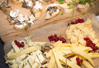 Cheese plate served with berries and nuts on a paper surface and wooden background