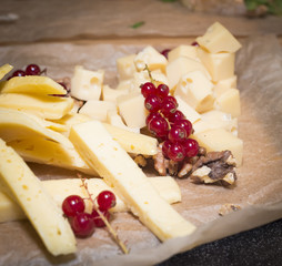 Cheese plate served with berries and nuts on a paper surface and wooden background