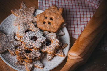 Homemade Christmas gingerbread and linzer cookies with jam, powdered, kitchen towel and rolling pin, top flat view, soft haze effect, vintage