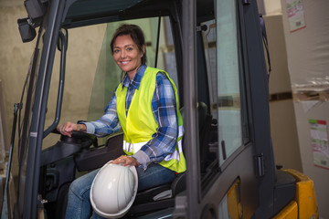 Woman posing on a forklift in a warehouse.
