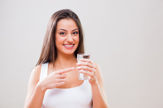 Portrait of young woman who is pointing at glass of water. Refreshment is important.