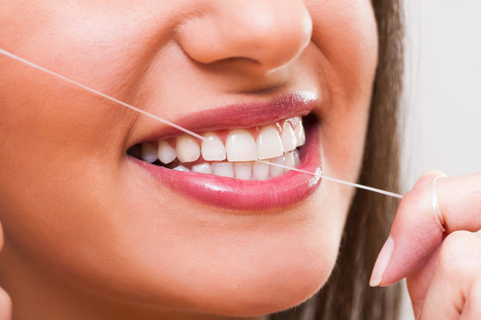 Close up image of young woman who is using dental floss.
