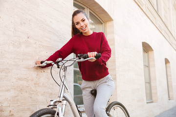 Young happy woman dressed in sweater walking with bicycle