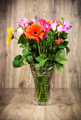 Mixed beautiful flowers in the vase on wooden background