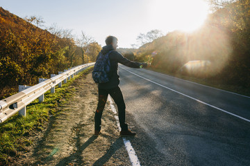 Man hitchhiking on a country road. Traveler showing thumb up on for hitchhiking during road trip. Adventure and tourism concept.