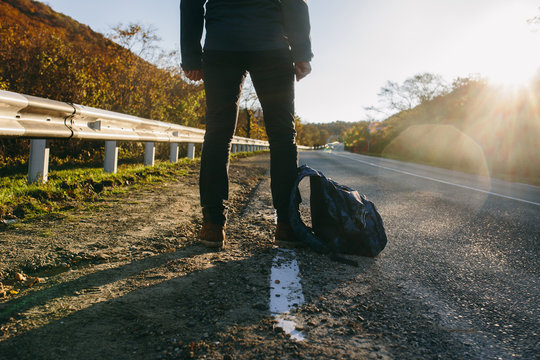 Man hitchhiking on a country road. Traveler showing thumb up on for hitchhiking during road trip. Adventure and tourism concept.