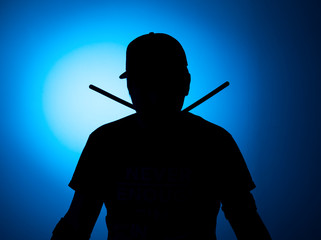 silhouette Expressive young drummer with drum stick on a blue background