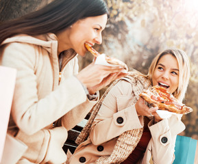 Friends eating pizza. Two young women eating pizza after shoppin