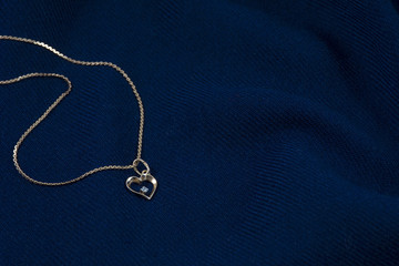Fototapeta na wymiar One golden chain with pendant in form of heart on the deep blue background
