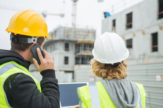 Two workers on a construction site using a tablet and a smartphone