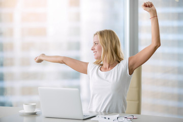 Young attractive woman at modern office desk, with laptop, stretching, getting a little exercise...