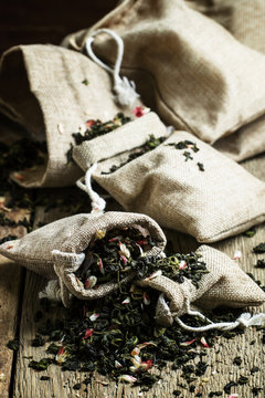 Dry green tea with petals of cherry, vintage wooden background,