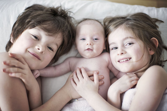 Boy and girl lying on bed with baby brother, portrait