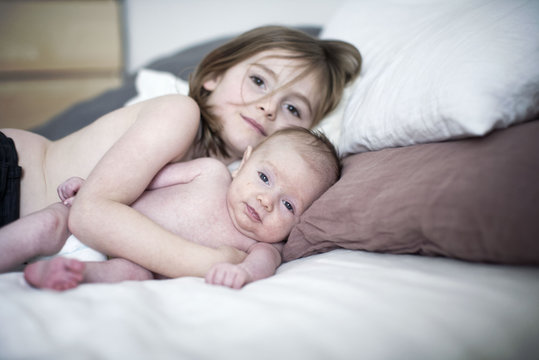 Little girl lying on bed with baby brother