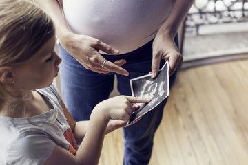 Mother using ultrasound photo to prepare daughter for imminent arrival of new sibling