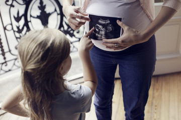 Mother using ultrasound photo to prepare daughter for imminent arrival of new sibling