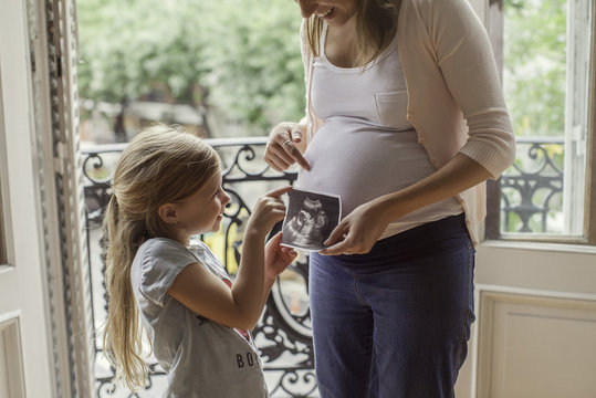 Mother using ultrasound photo to prepare daughter for imminent arrival of new sibling