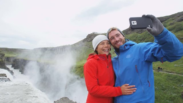 Travel couple fun taking selfie photo by Dettifoss waterfall on Iceland using smart phone. People visiting famous tourist attractions and landmarks on Diamond Circle. RED EPIC SLOW MOTION 96 FPS.