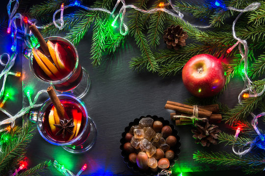 Hot Mulled wine with cinnamon, garland and christmas tree on black slate dish. Top view and copy space.