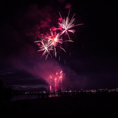 People watching colorful fireworks above the river