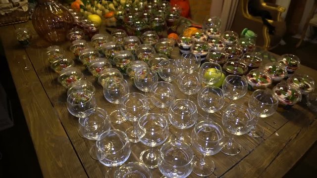 Vegetarian food in plastic cups and empty wine glasses on a large wooden table