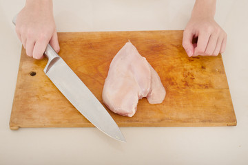 chicken breast on wooden board with female hands and knife
