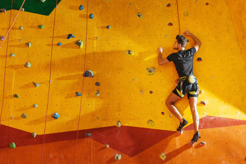 Young man climbing up the wall with equipment