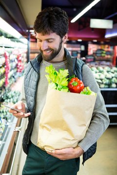 Man using mobile phone while holding grocery bag