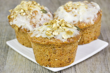 Three small carrot cakes on a white plate on a wooden table.