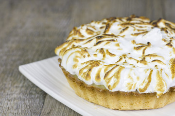Small lemon pie on a white plate on a wooden table.