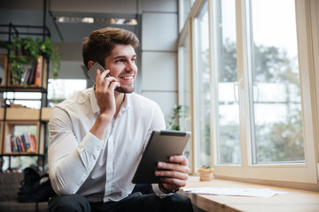 Smiling businessman using tablet computer while talking by phone