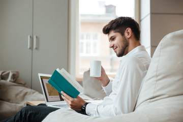 Joyful businessman drinking tea while reading book.
