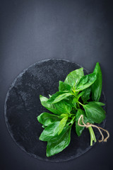 Fresh bunch of basil on the black slate plate background. Top view. Selective focus.