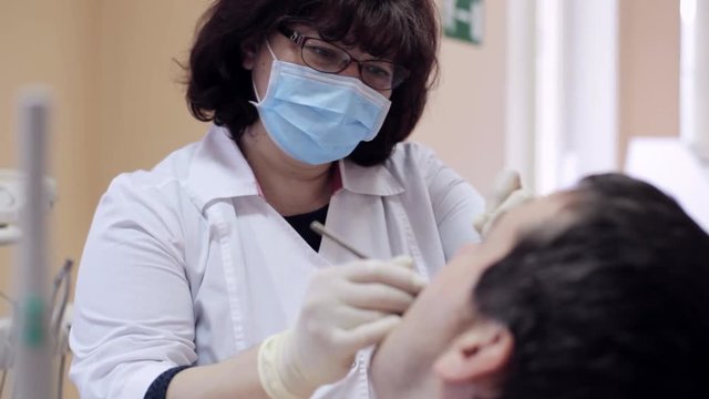 Dentist checks teeth of male patient by dental mirror