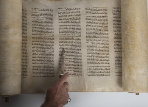 hand of a man reading an ancient torah scroll
