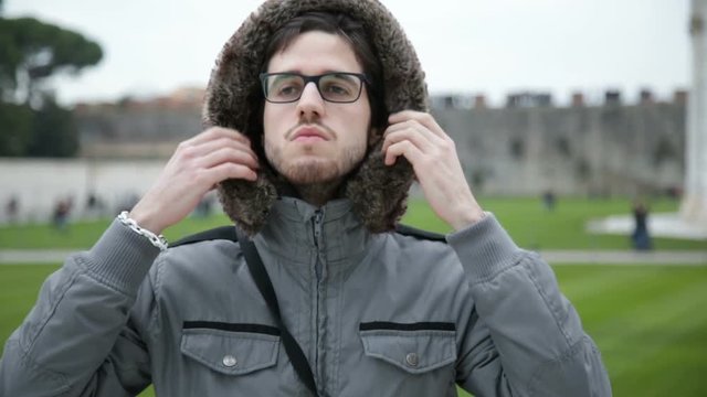 Ragazzo con giacca grigia si sta mettendo il cappuccio in Inverno.