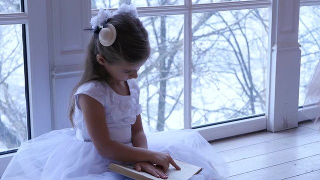 Child sits on the floor and reading a book near the window at home