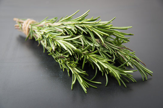 Sprigs of rosemary tied with string on a dark black background.