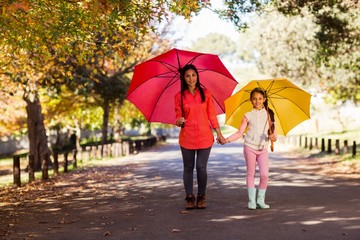 Mother and daughter holding umbrellas on street at park