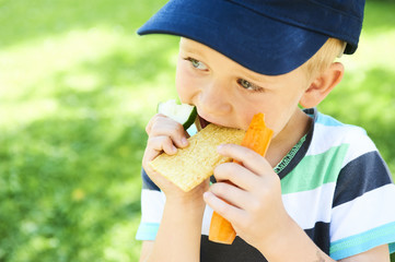 Child little boy eating crispbread and vegetable outside in the summer park