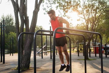 Fit man doing triceps dips on parallel bars at park exercising outdoors
