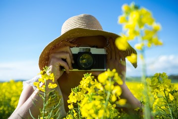 Woman taking picture from camera in mustard field