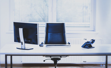 Modern empty office space desk with computer, phone and chair.