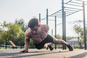 Athlete young man doing one-arm push-up exercise working out his upper body muscles outside in summer.