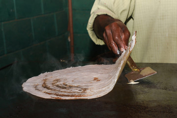 making or cooking in traditional kitchen. dosa is a fermented crepe made from rice batter and black...